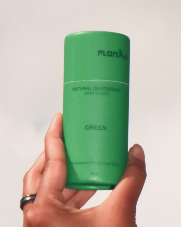 Hand holding a tube of Monks Green Natural Deodorant against a cloudy sky.