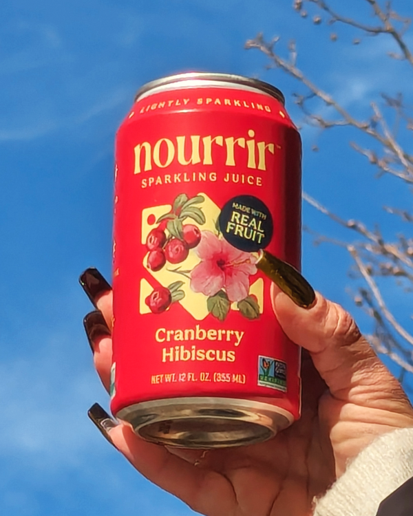 Hand holding NOURRIR - Cranberry Hibiscus Sparkling Juice in the air