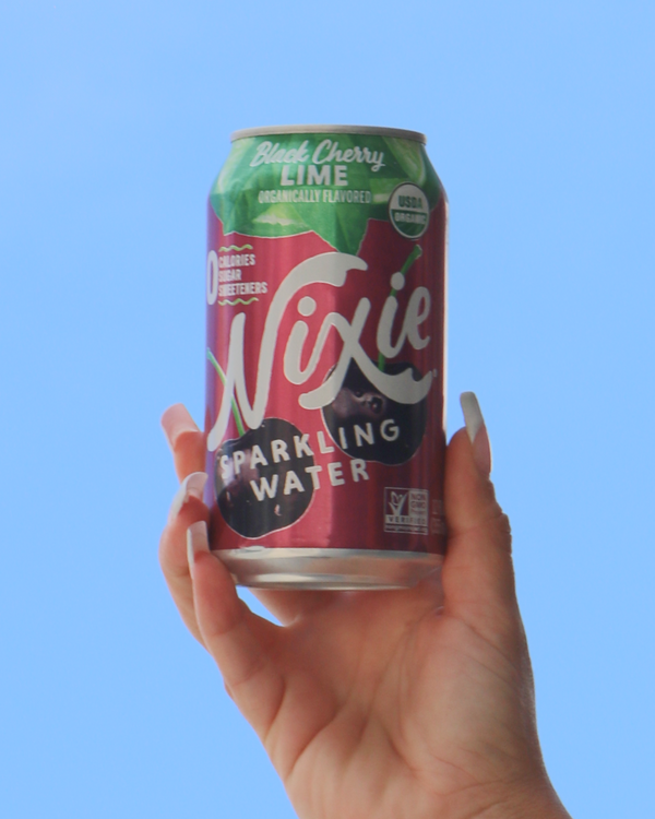 Hand holding a can of Nixie Black Cherry Lime sparkling water against a blue background