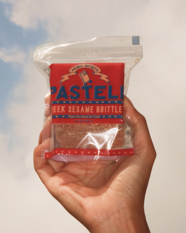 Hand holding a package of Pasteli Greek Sesame Brittle against a blue sky.